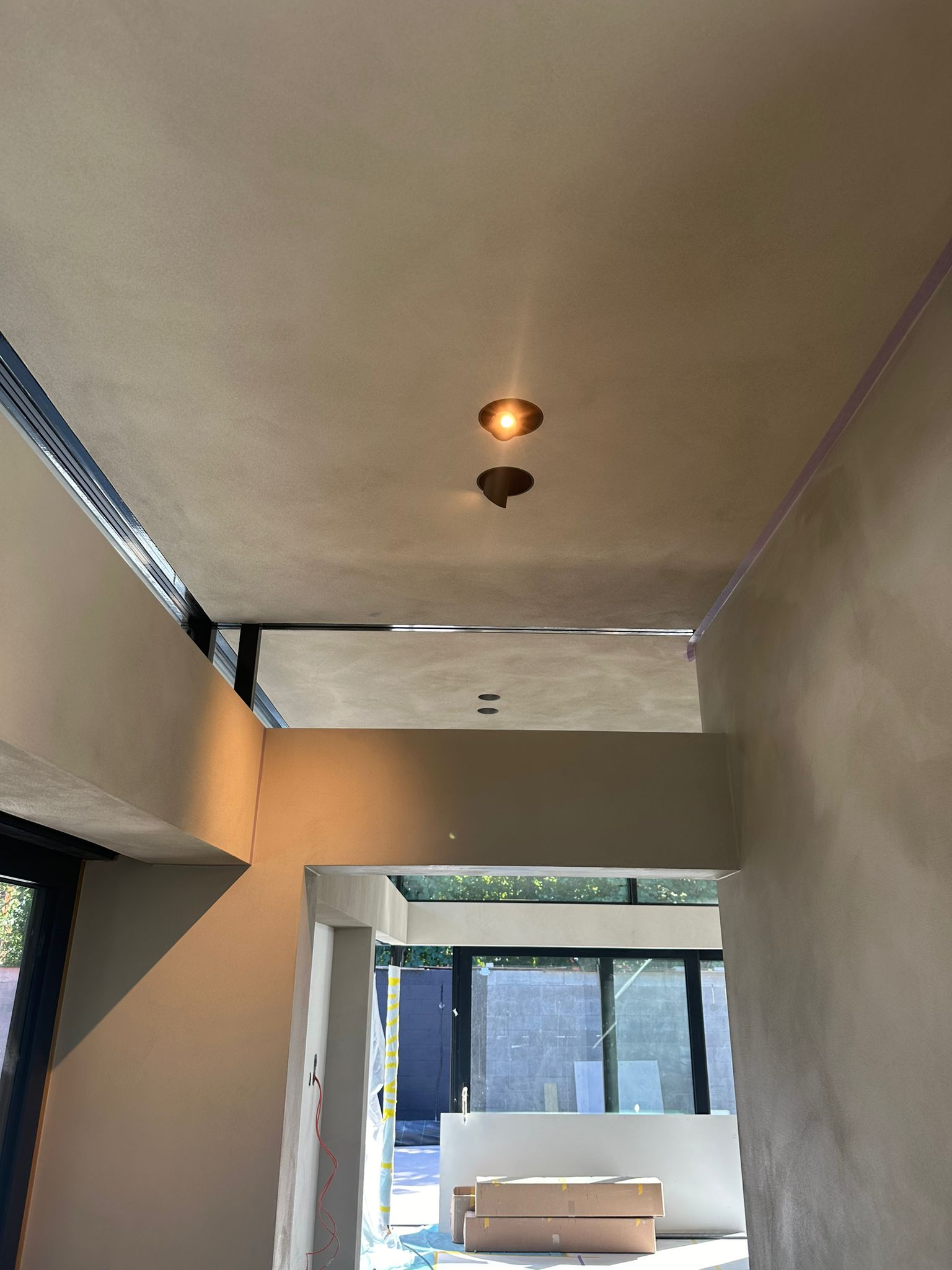 Gestuct plafond in de afbouwfase met uitsparingen voor inbouwspots en inbouwspeakers, uitzicht op de tuin
