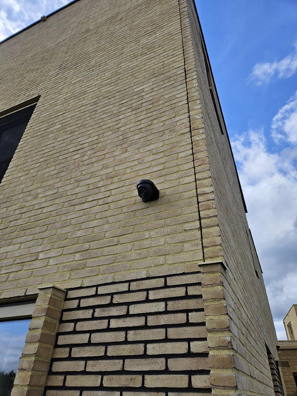 Zwarte dome-camera gemonteerd hoog op een lichte bakstenen gevelhoek van een woonhuis