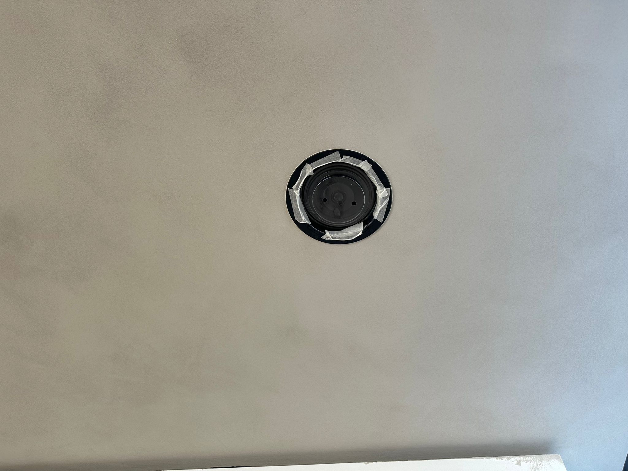 Close-up van een ronde zwarte inbouwspeaker die strak in het plafond is weggewerkt en afgeplakt
