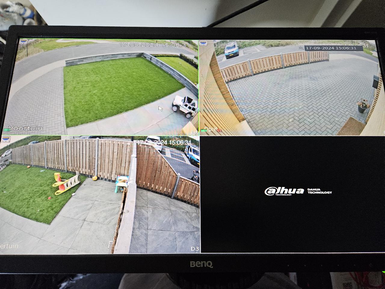Monitor met vier vlakken die de drie camerabeelden van de woning tonen: voortuin, oprit en achtertuin, plus het Dahua-logo