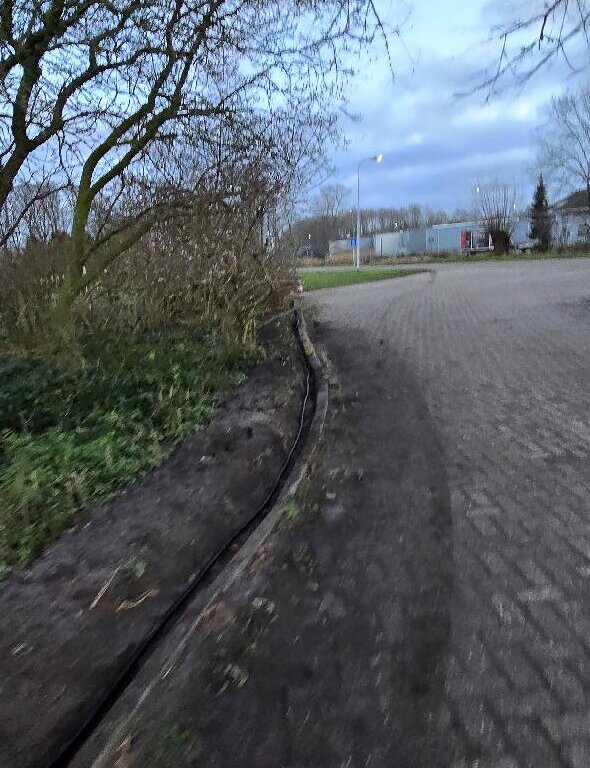 Uitgegraven sleuf met kabelbuis langs een bestraat bedrijventerrein