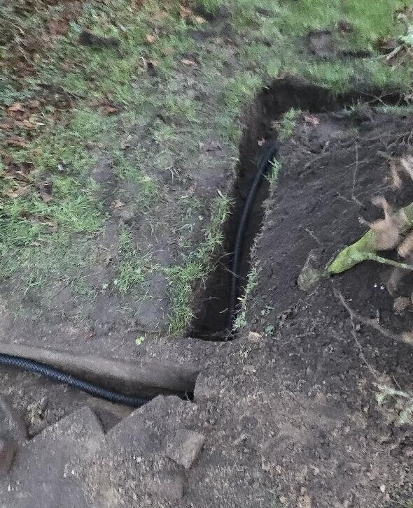 Zwarte kabelbuis in een uitgegraven sleuf door een grasveld voor de camerabekabeling