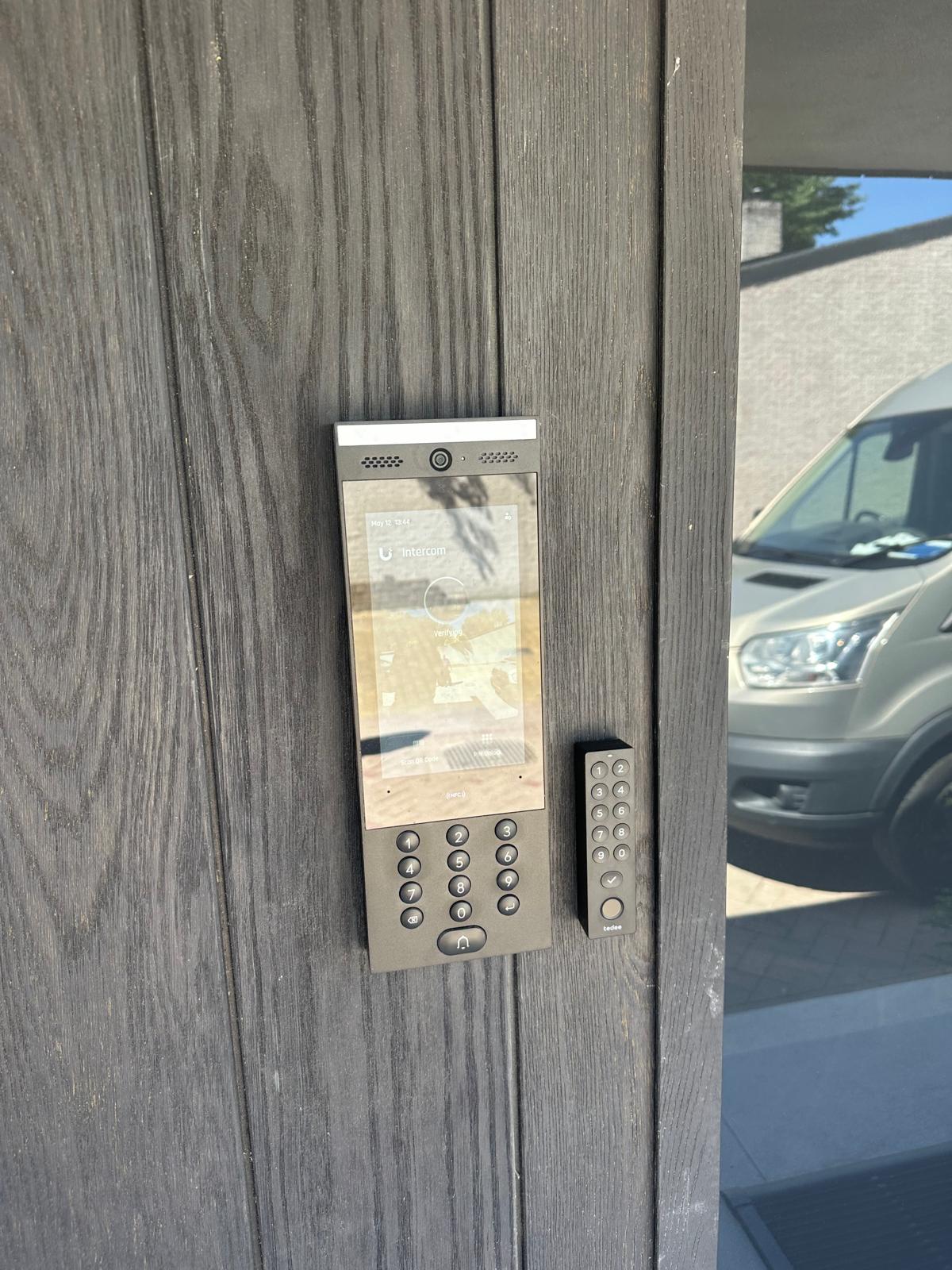 UniFi Access deurstation met touchscreen en keypad naast een tedee-keypad, vlak in donkere houten gevelbekleding