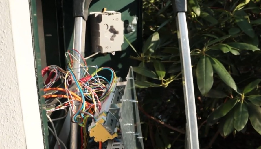 Open kabelkoker met een bundel gekleurde bekabeling en een kabelgoot bij een toegangspilaar
