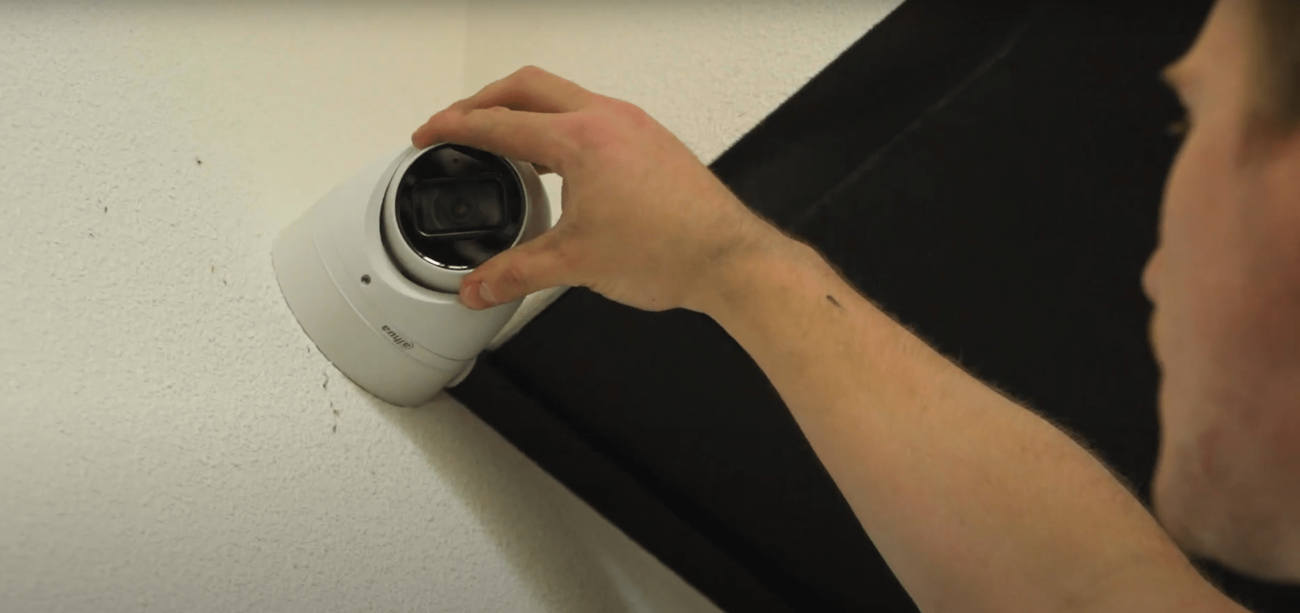 Monteur van CameraInstallatie stelt met de hand een witte Dahua-dome-camera af tegen een lichte wand