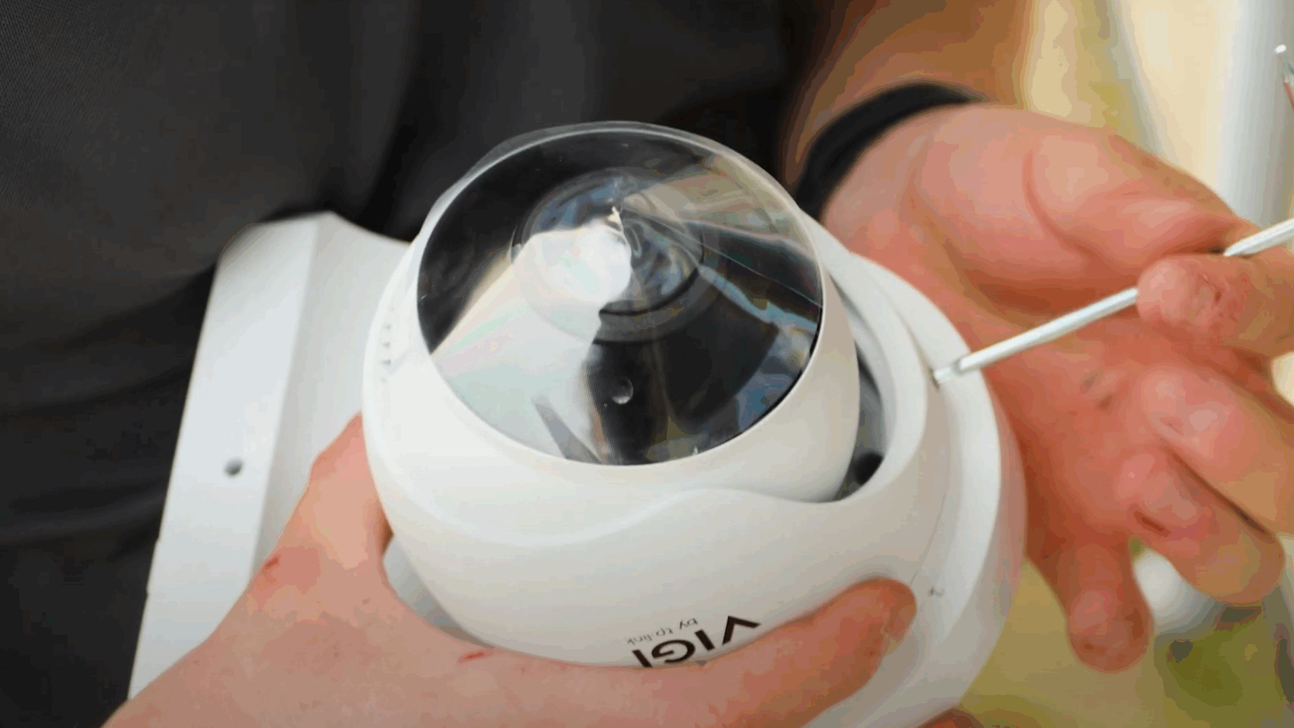 Handen van een monteur stellen een witte VIGI dome-camera met een schroevendraaier af tijdens de installatie
