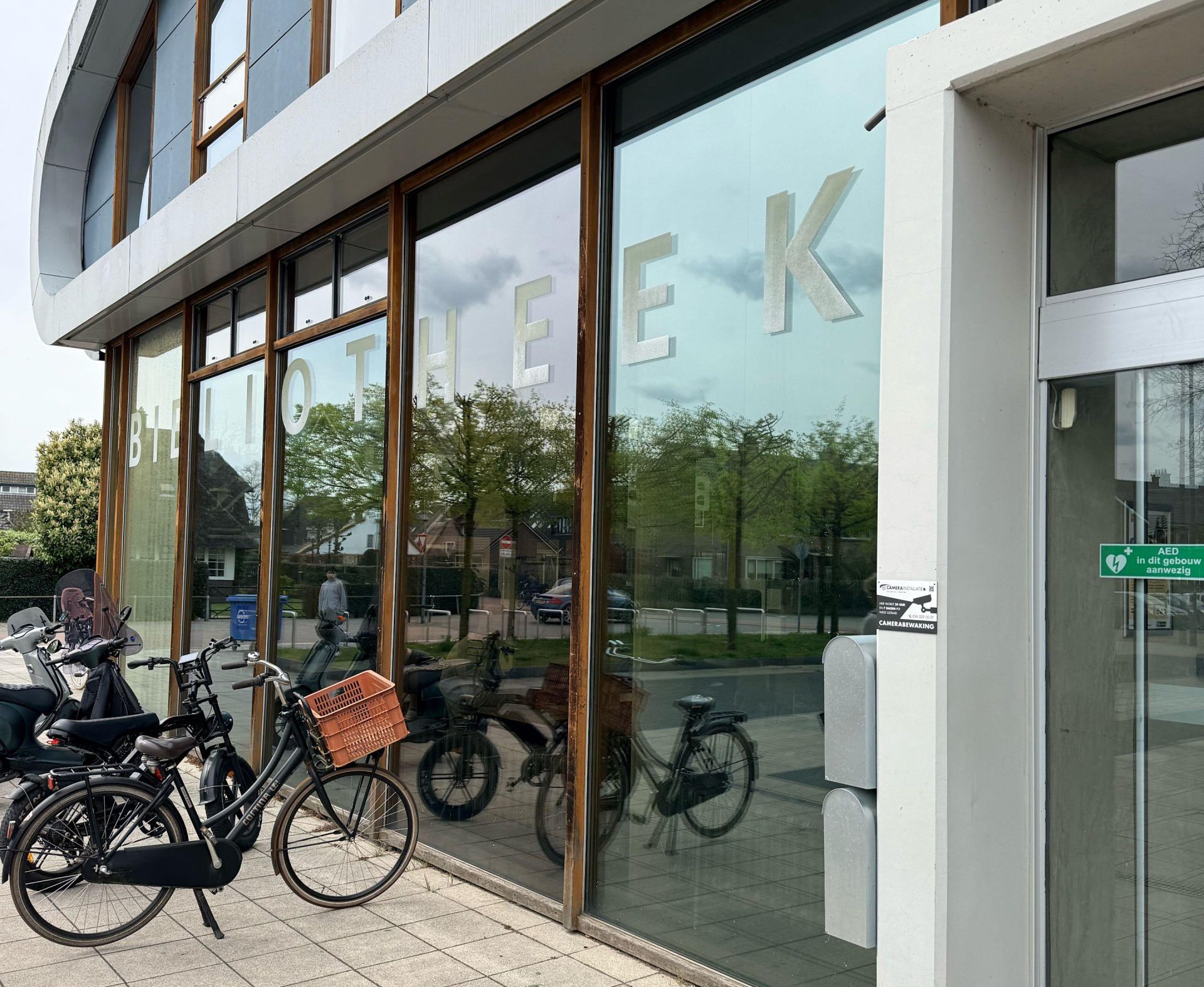 Glazen gevel van een bibliotheek met de letters BIBLIOTHEEK op de ruit en fietsen ervoor