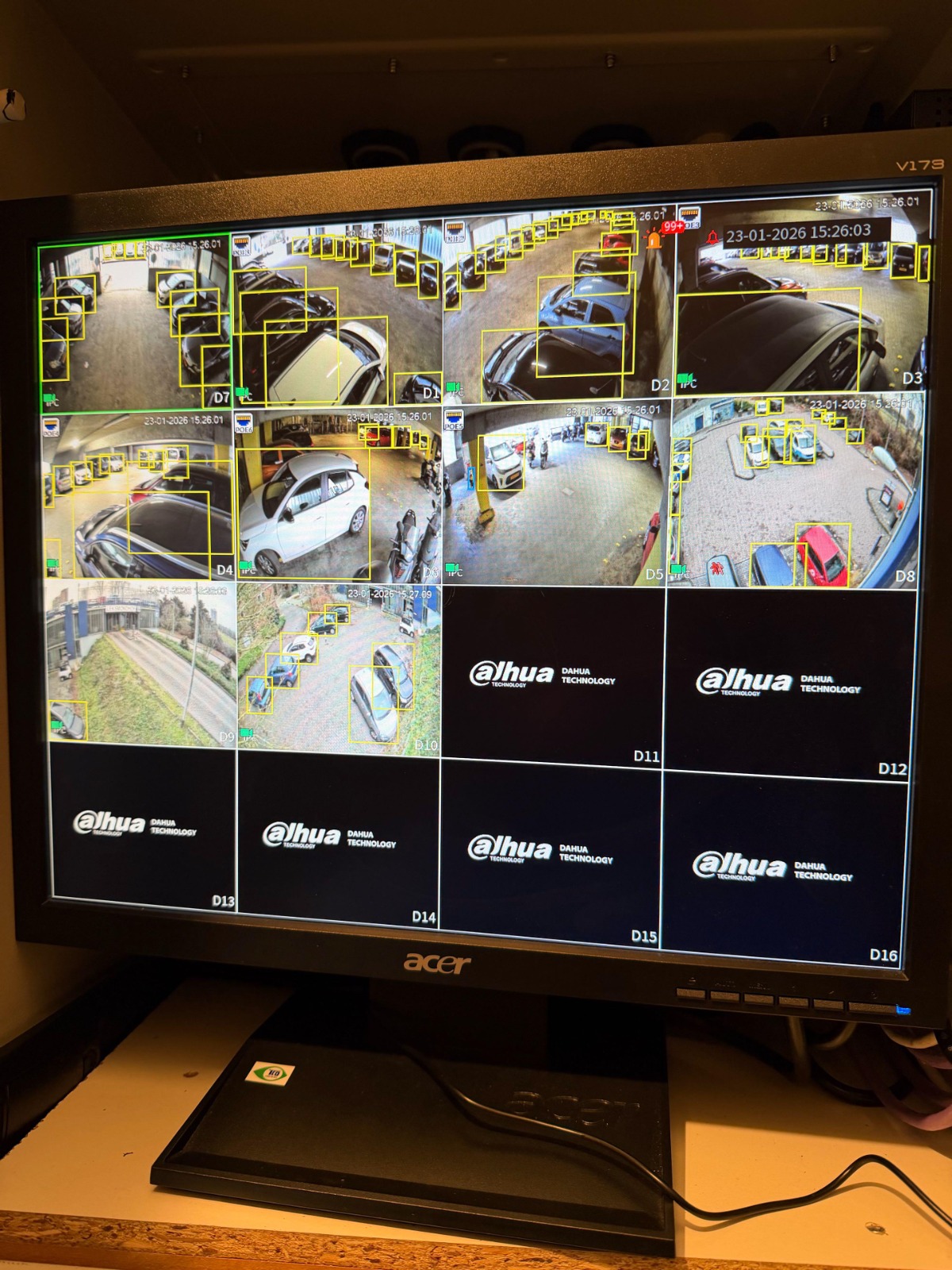 Recordermonitor toont een raster met live camerabeelden van het complex, met gele detectiekaders om personen en voertuigen