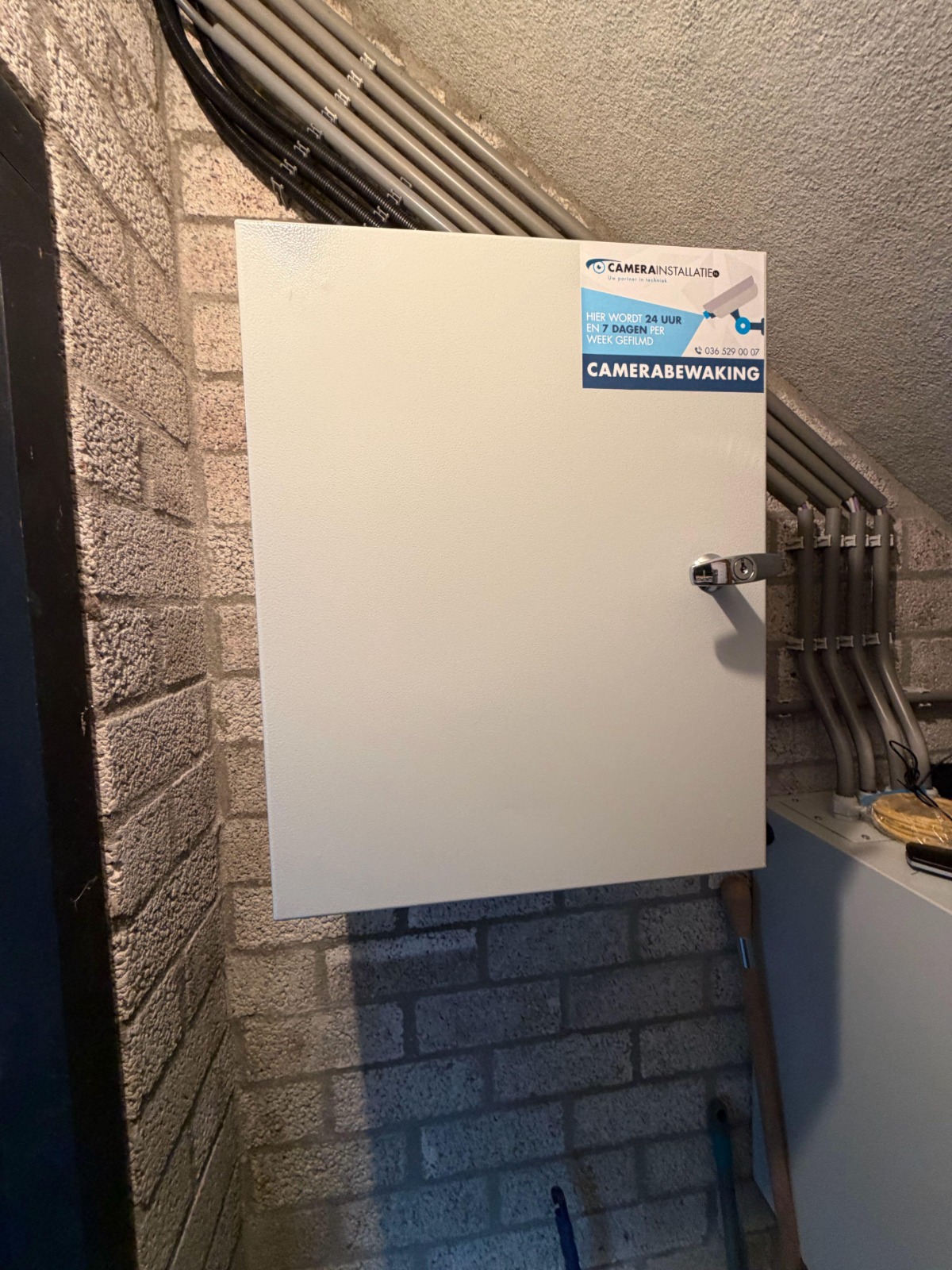 Nette wandkast van CameraInstallatie tegen een bakstenen muur, met keurig gebundelde kabelbuizen die ernaartoe lopen