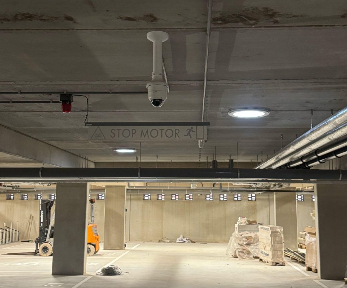 Camera op een verlengde plafondbeugel in de parkeergarage bij een STOP MOTOR-bord, met zicht over de lege parkeervakken