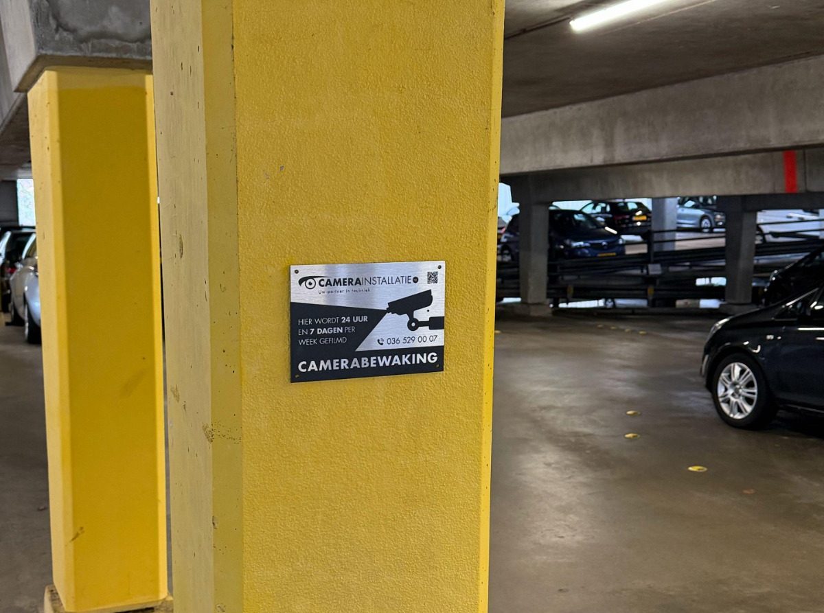 Bord van CameraInstallatie op een gele kolom in de parkeergarage: hier wordt 24 uur per dag gefilmd