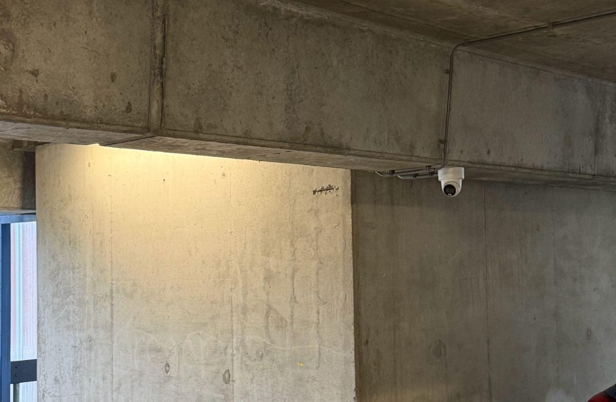 Witte turretcamera netjes gemonteerd tegen een betonnen balk in een gemeenschappelijke ruimte