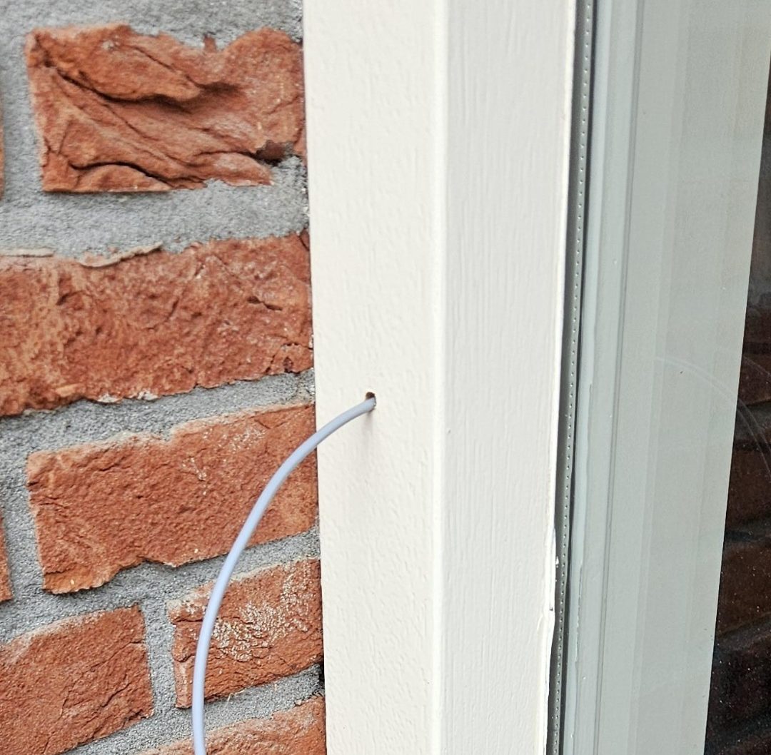 Kabel voor de deurbel wordt door een geboord gaatje in het witte deurkozijn naar binnen geleid