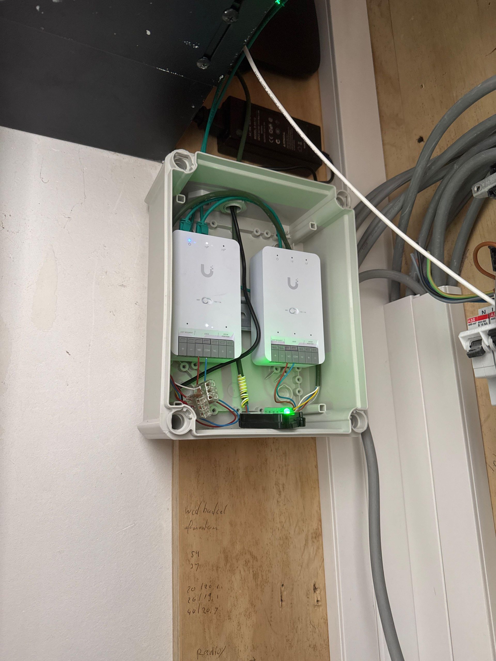 Twee witte UniFi Access-hubs in een waterdichte behuizing met bedrade LOCK- en EXIT-contacten voor de sloutaansturing