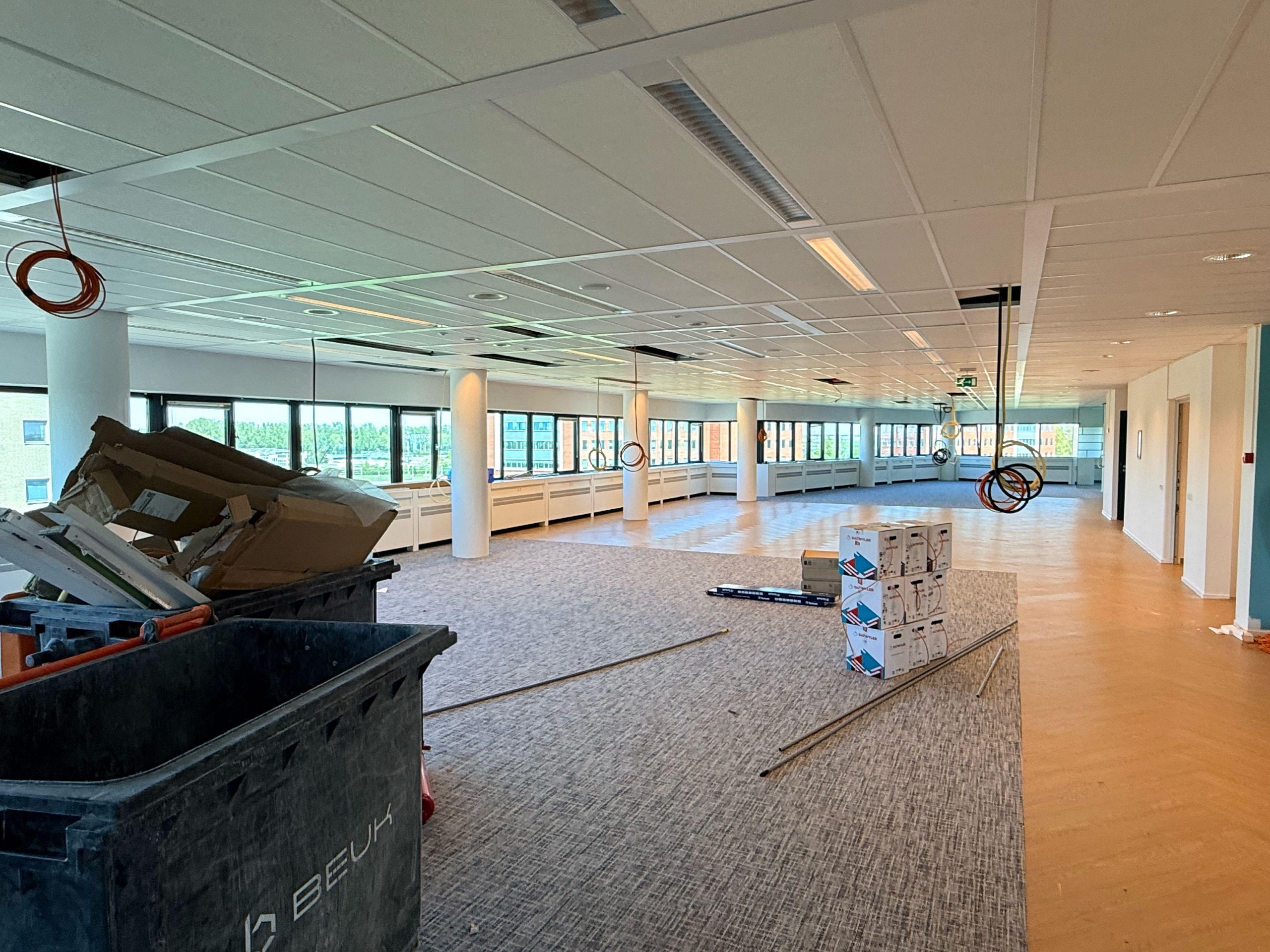 Ruime kantoorvloer in aanbouw met kabelrollen aan het plafond en stapels Datwyler-netwerkkabeldozen op de vloer