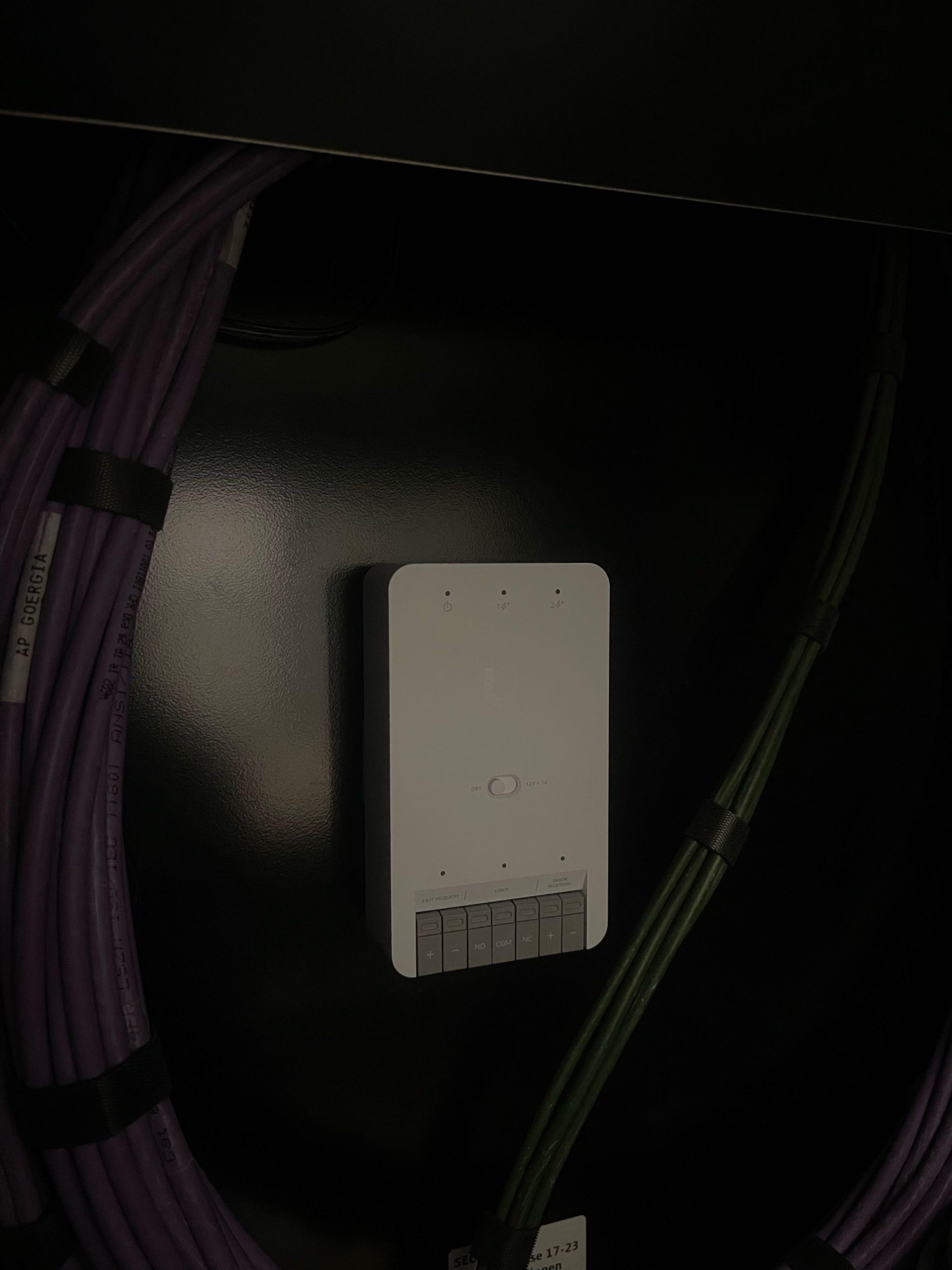 UniFi Access toegangsmodule met aansluitingen voor slot en deurcontact, gemonteerd in het rack tussen gelabelde datakabels
