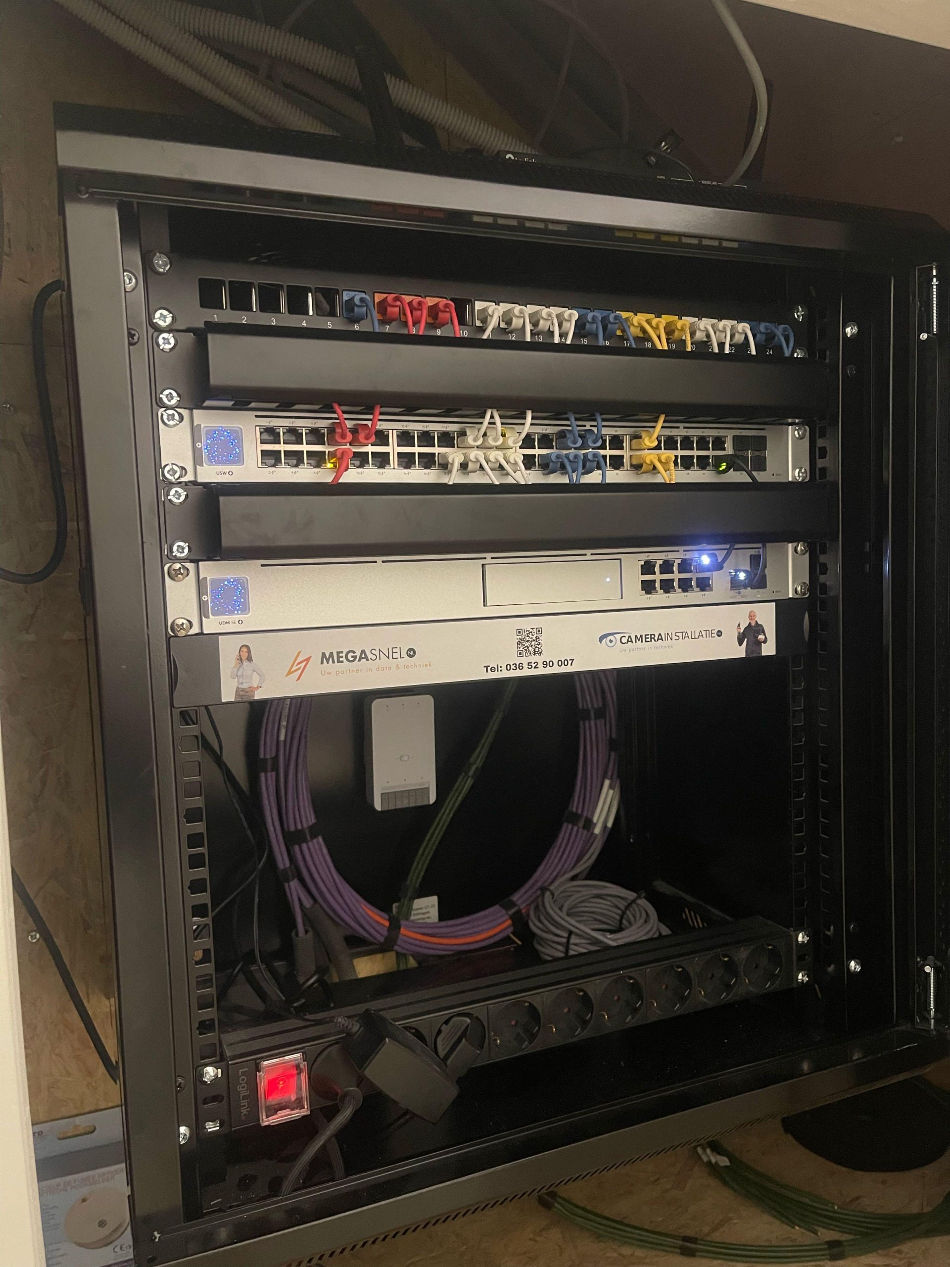 Open netwerkrack met patchpaneel, UniFi USW-switch en UDM SE, met een gelabelde strip van MegaSnel en CameraInstallatie
