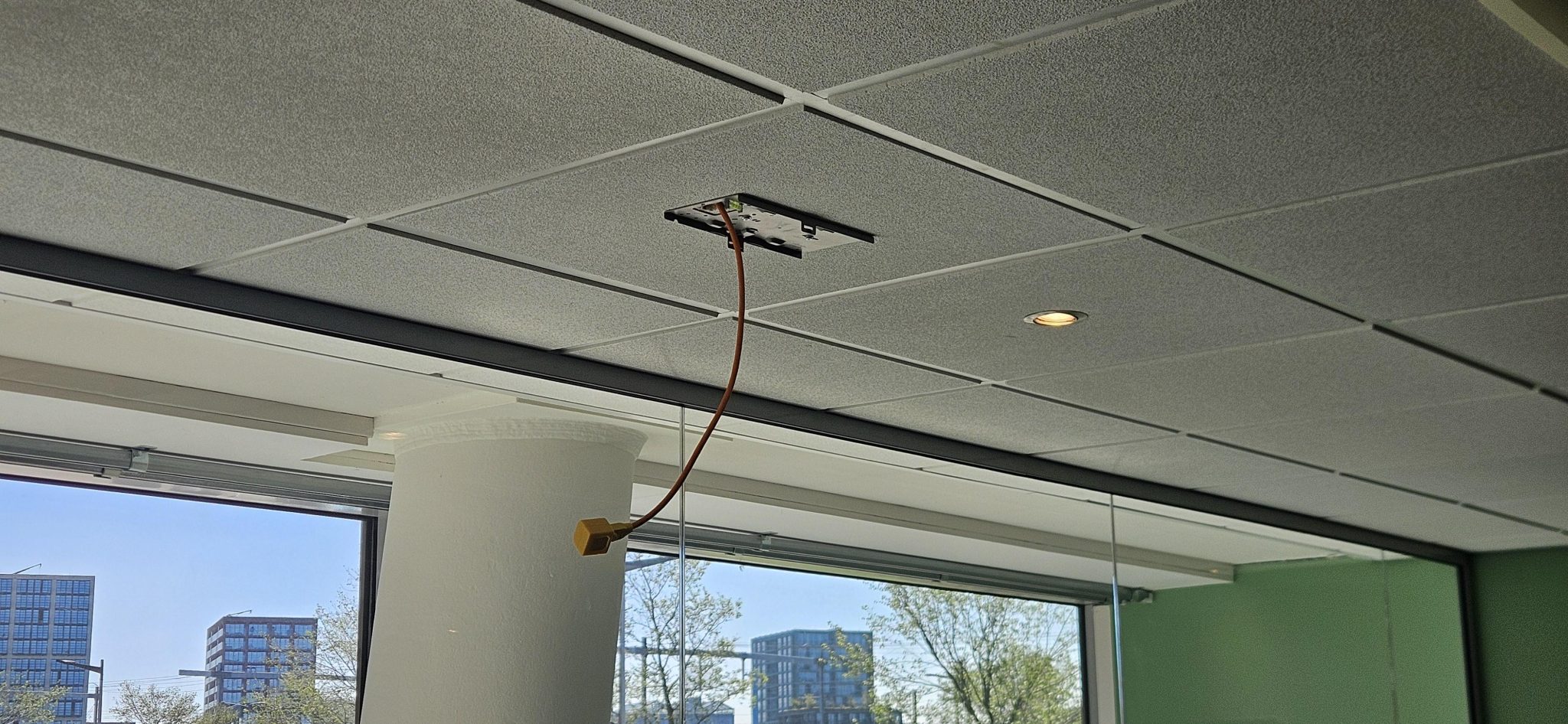 Montagebeugel voor een plafond-access point met een oranje netwerkkabel die door de systeemplafondtegel naar beneden komt