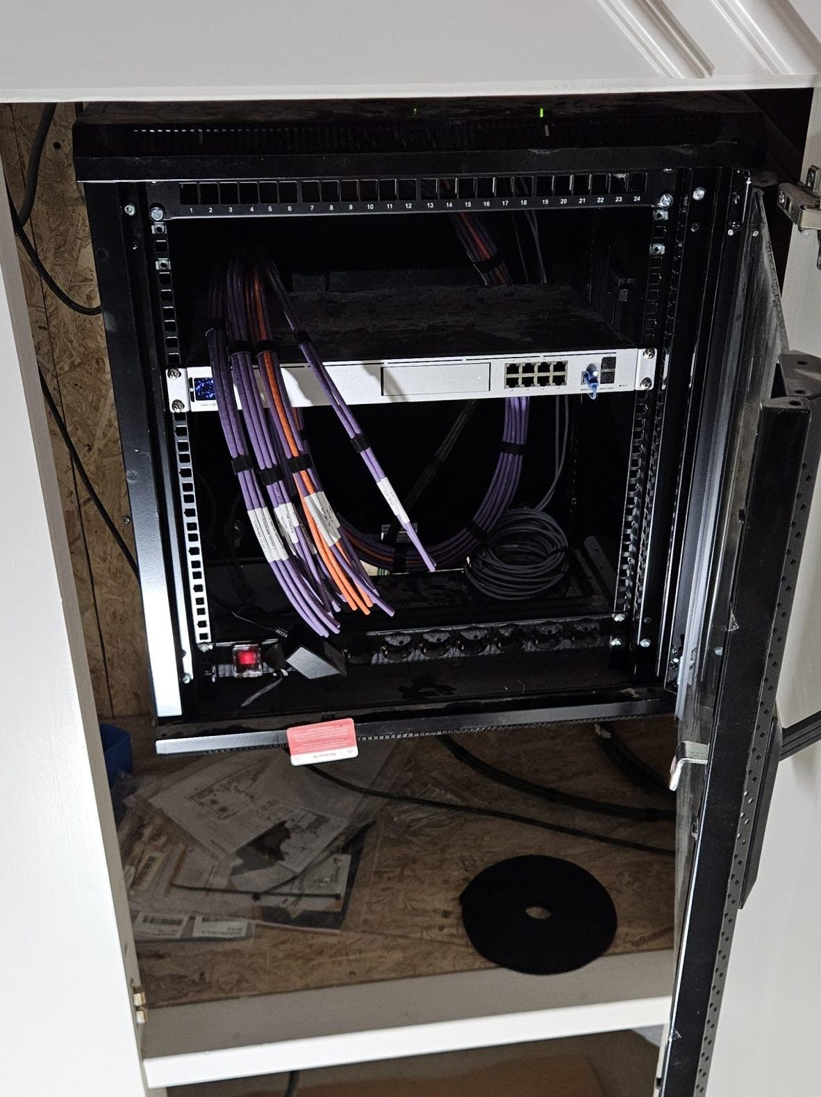 Open netwerkkast in de woning met een UniFi-switch en netjes opgerolde, gelabelde paarse en oranje datakabels