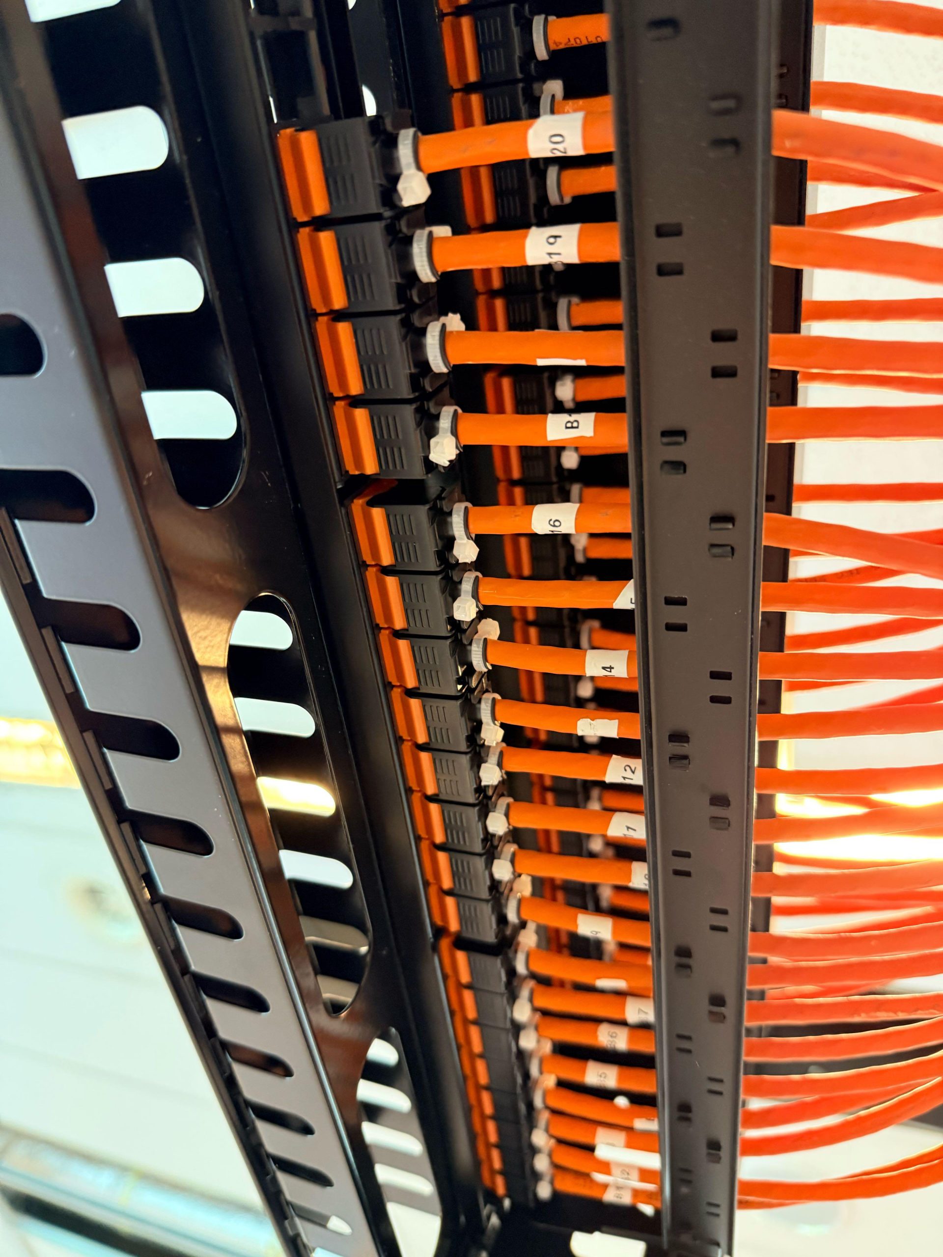 Oranje netwerkkabels netjes genummerd met labels 12, 16, 19 en 20 in de kabelgeleiding van de rack
