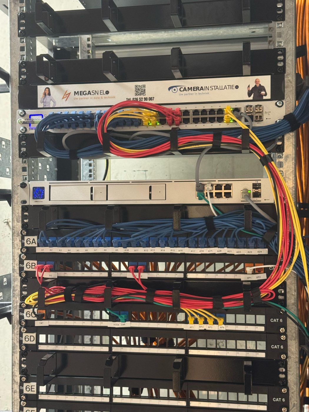 Professioneel ingerichte netwerkkast met UniFi-gateway, managed switch en genummerde patchpanelen, met een label van CameraInstallatie.nl en MegaSnel