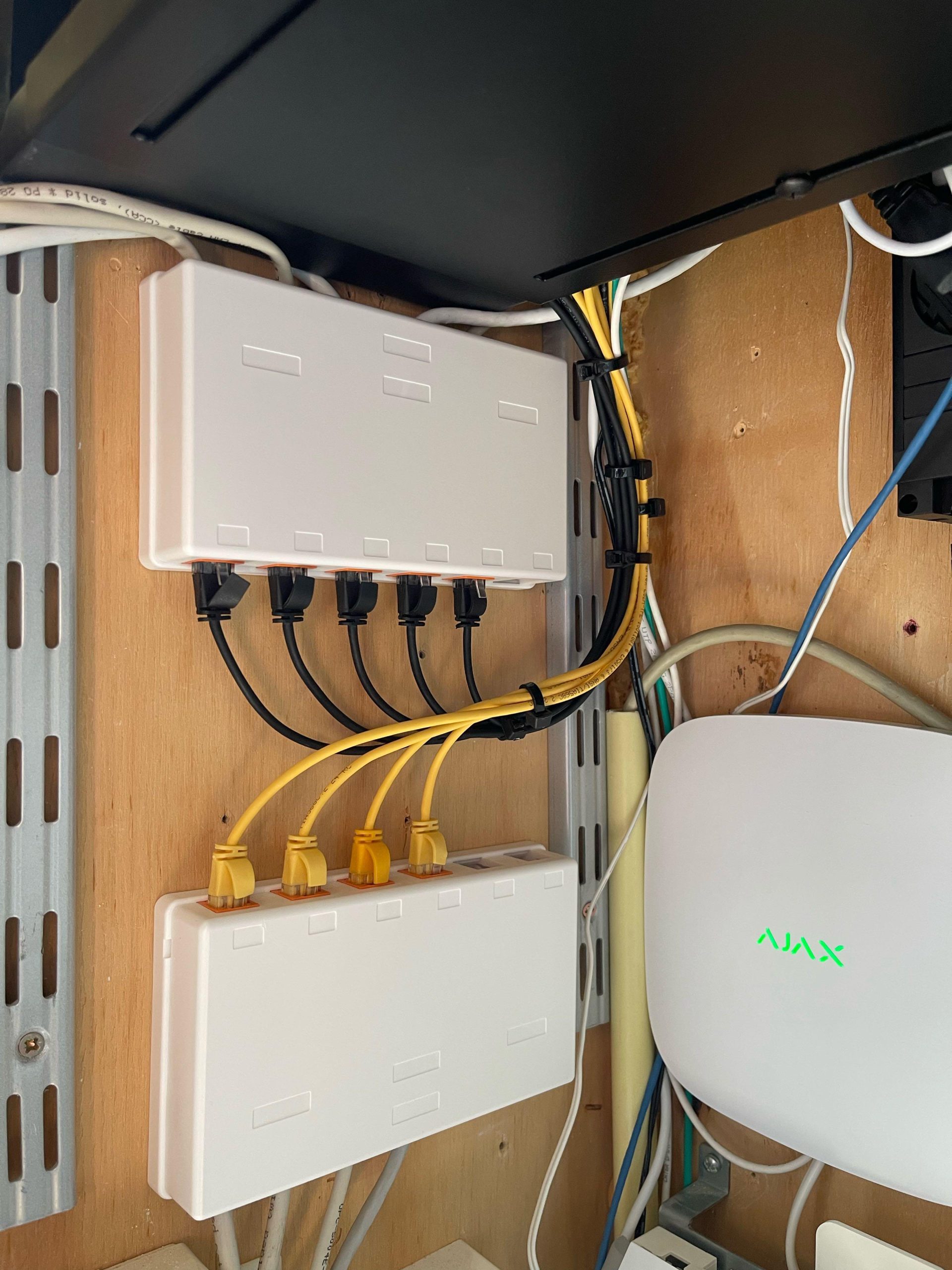 Netwerkkast met witte patchpanelen, geel en zwart UTP-patchwerk en een witte Ajax Hub in de meterkast