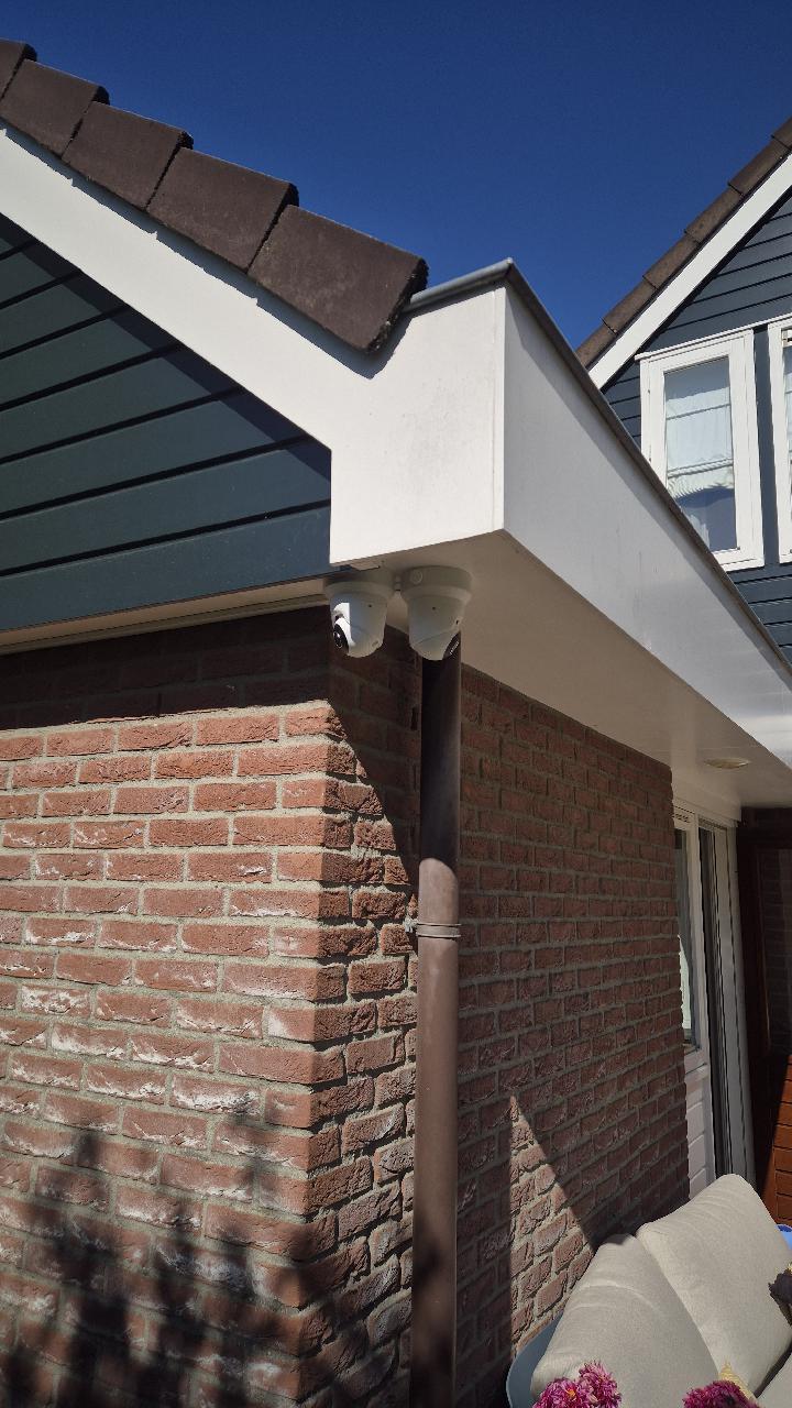 Twee witte Ajax dome-camera's gemonteerd onder een witte dakrand op de hoek van een bakstenen woning
