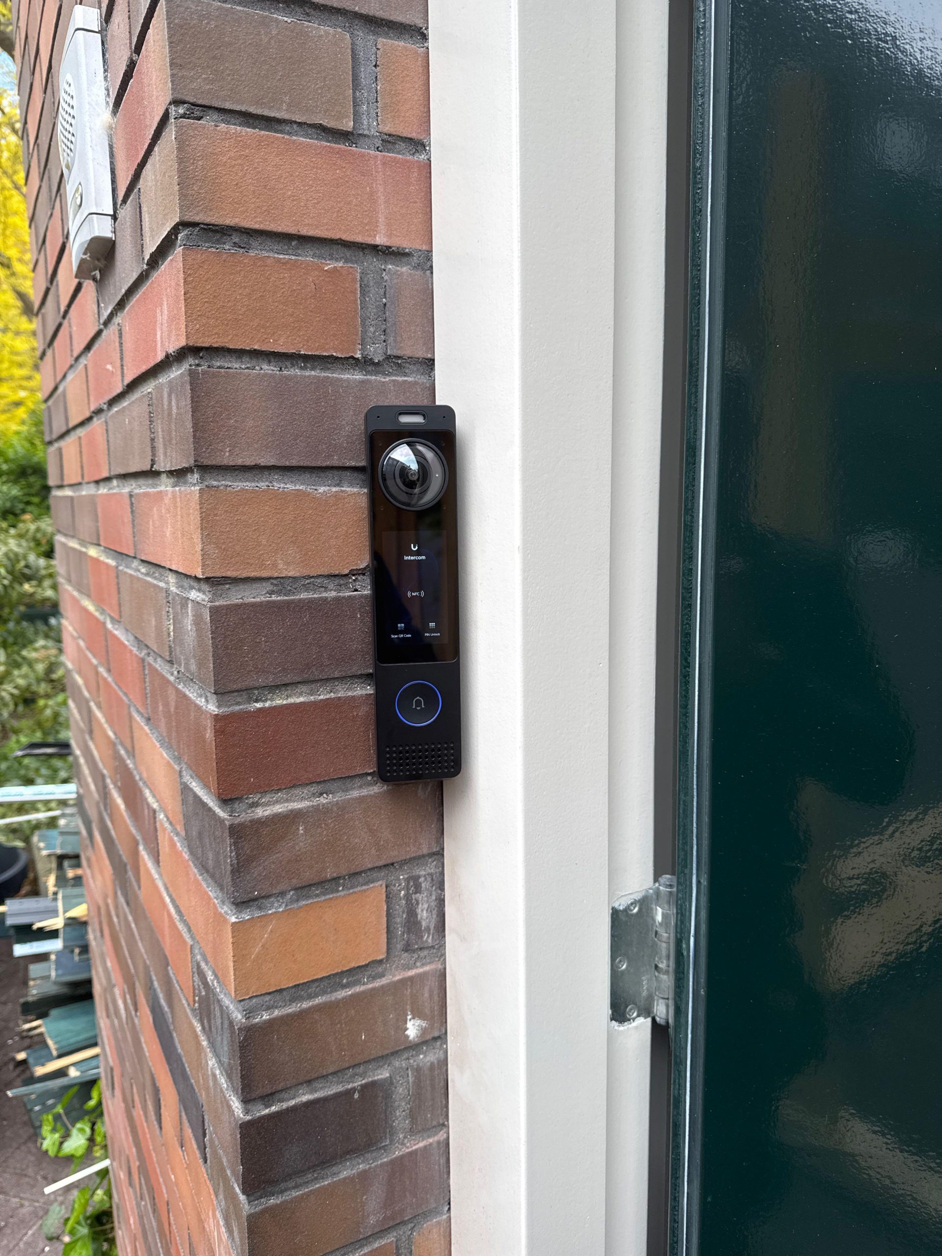 Compacte UniFi-intercom met camera en scherm gemonteerd op het kozijn naast een groene voordeur