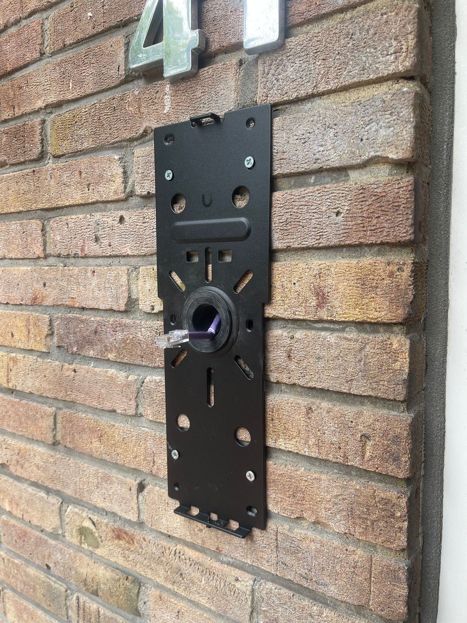 Montageplaat van een nieuwe video-intercom vastgezet op de bakstenen gevel, met de bestaande kabel al door de opening getrokken