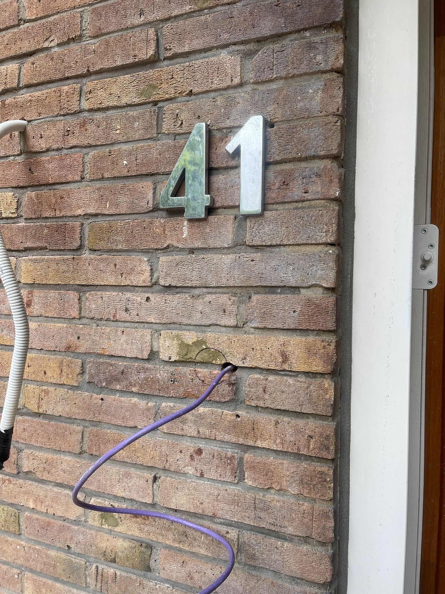 Paarse netwerkkabel die door een geboord gat in de bakstenen muur naar het toegangspunt bij de voordeur loopt