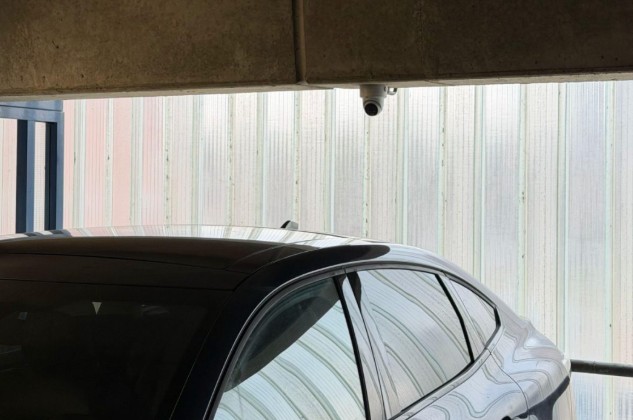 Domecamera onder een afdak met daaronder een geparkeerde auto