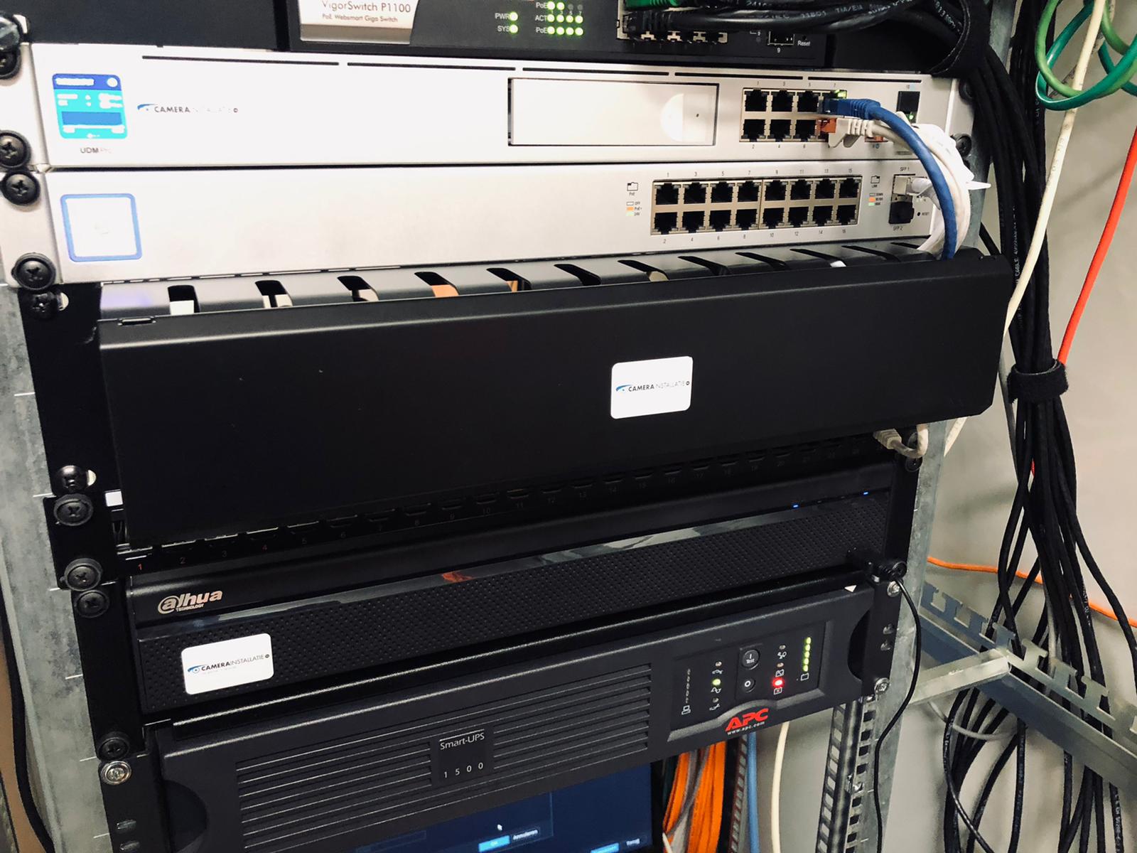 Close-up in een serverrack van ons eigen werk: bovenin twee netwerkswitches met aangesloten patchkabels, daaronder een blind paneel, een recorder en onderin de noodstroomvoorziening