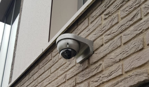 Domecamera aan een bakstenen gevel, gespoten in een tint die opgaat in de kleur van de muur in plaats van standaard wit