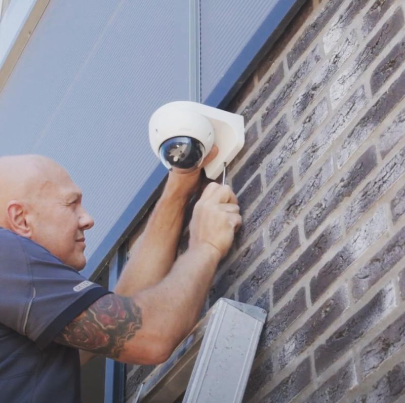 Monteur van CameraInstallatie schroeft een camera netjes vast aan de gevel nadat de kabel is weggewerkt