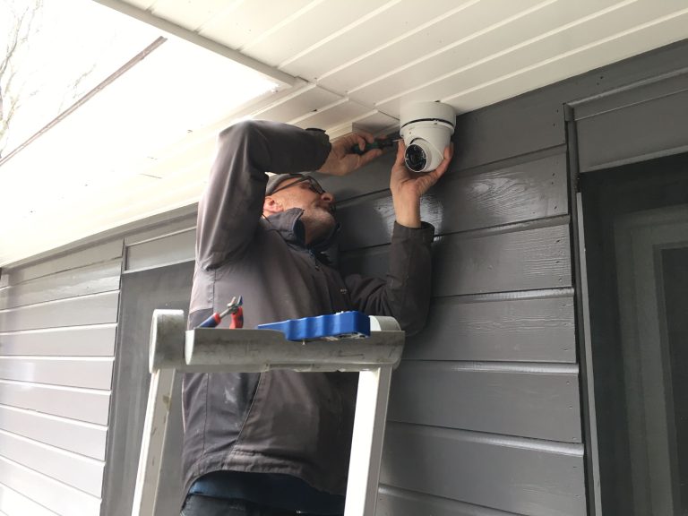 Monteur van CameraInstallatie monteert een dome-camera onder een overkapping bij een voordeur
