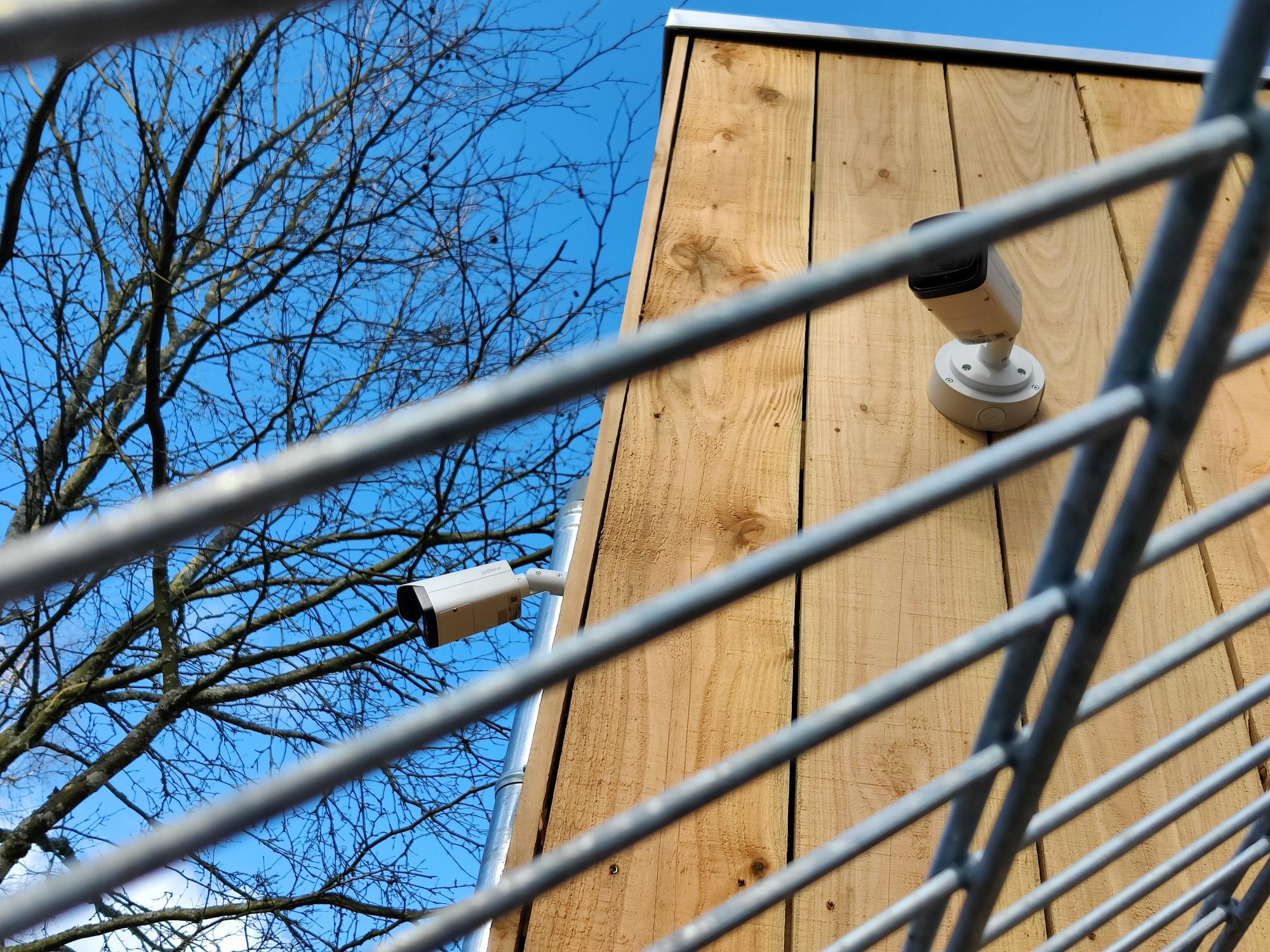 Camera aan een houten wand achter het hekwerk van een terrein