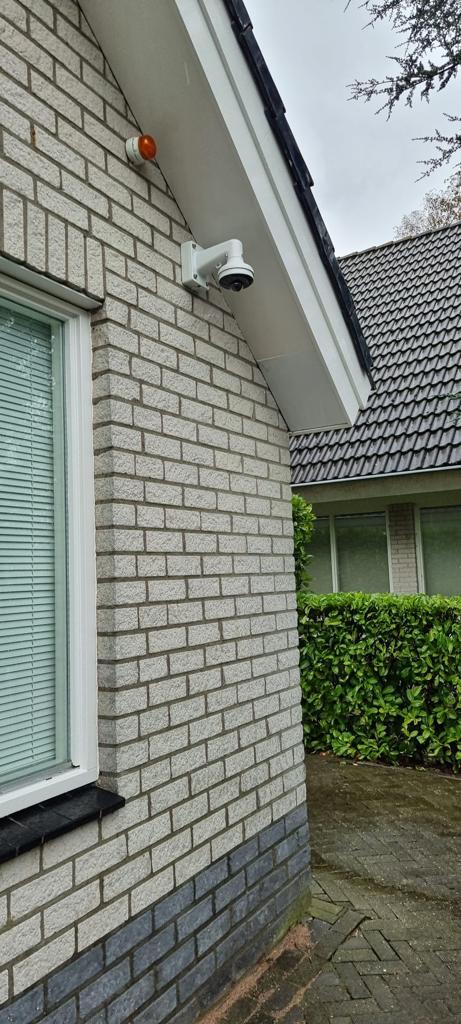 Witte domecamera onder de dakrand aan de lichte gevel van een woning, gericht op de oprit
