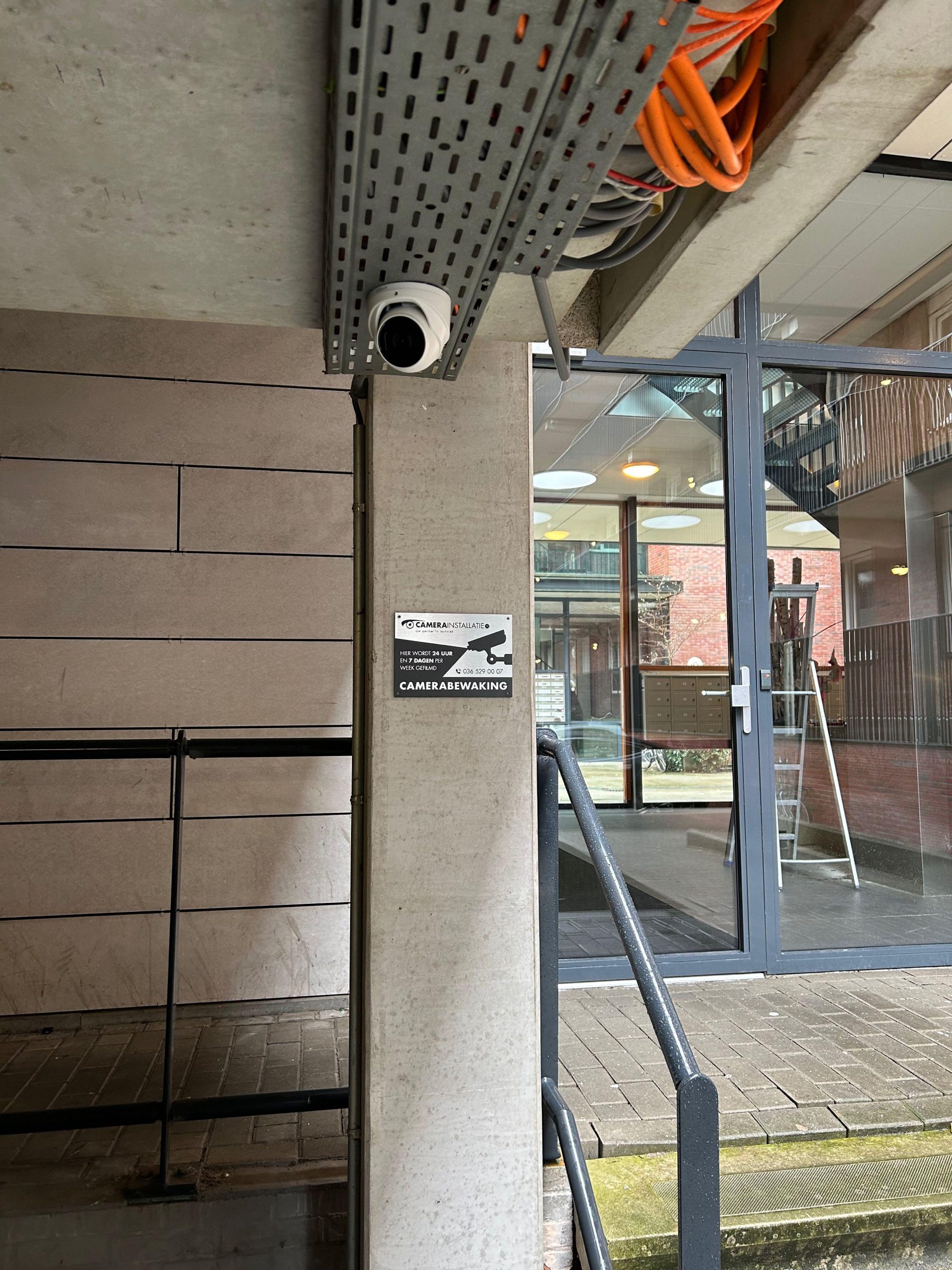 Camera onder een kabelgoot bij de overdekte entree, met CameraInstallatie-bord
