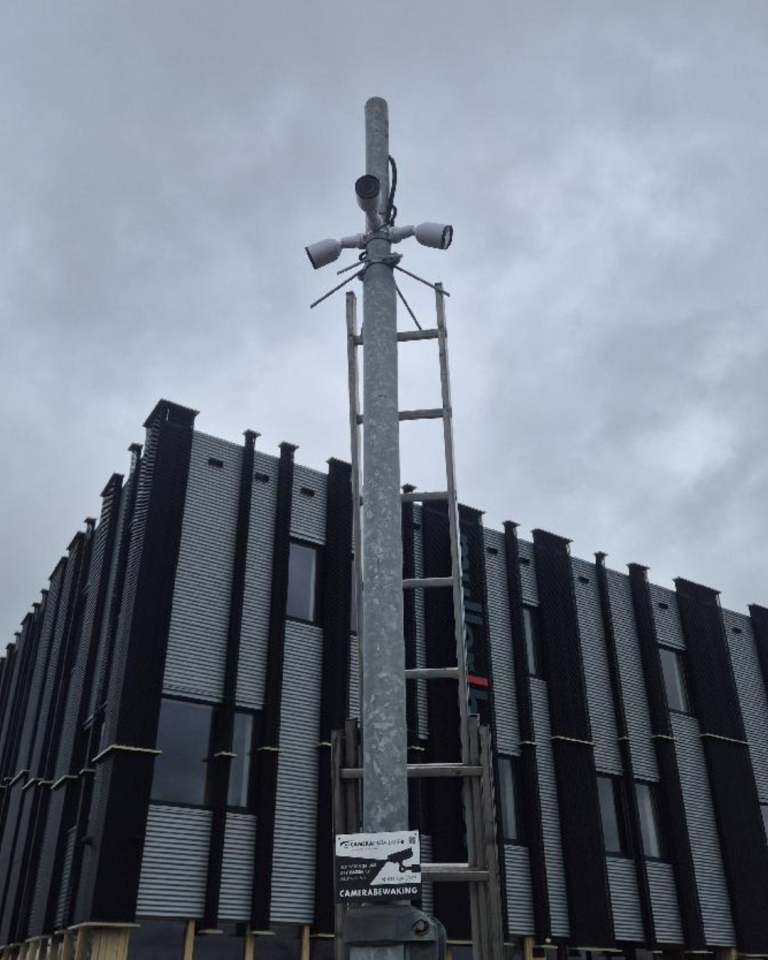 Cameramast met antennes naast een nieuwbouwpand