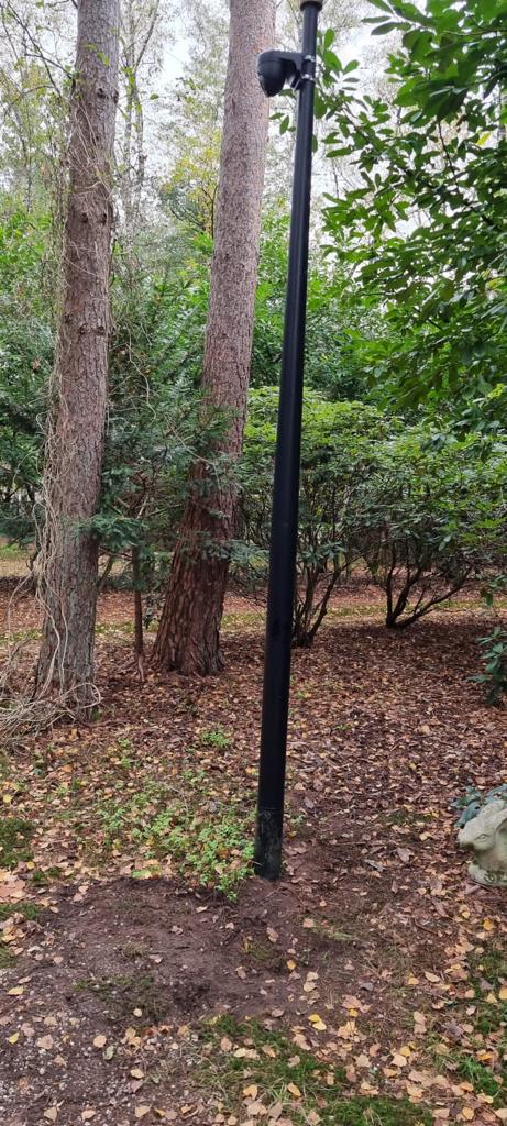 Zwarte camerapaal net geplaatst in de grond, met verse aarde rond de voet