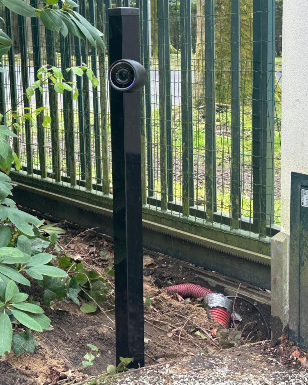 Beveiligingscamera op een zwarte paal bij de erfgrens naast een hek