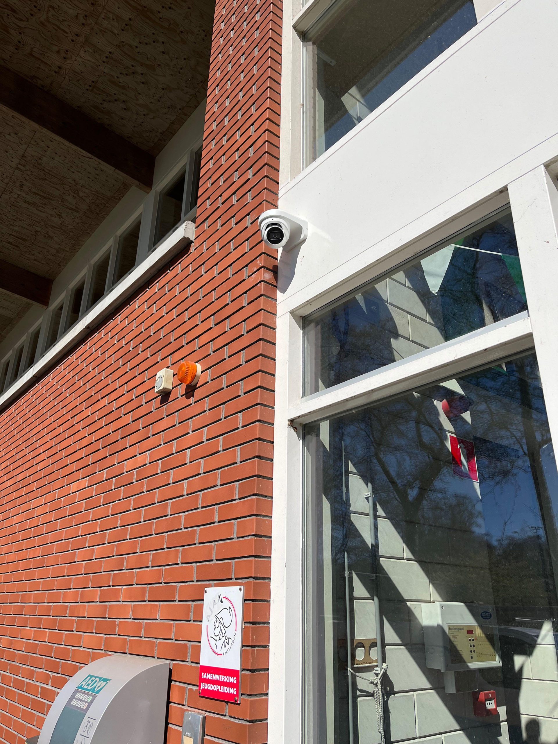 Witte camera op de hoek van een pand naast de glazen entree