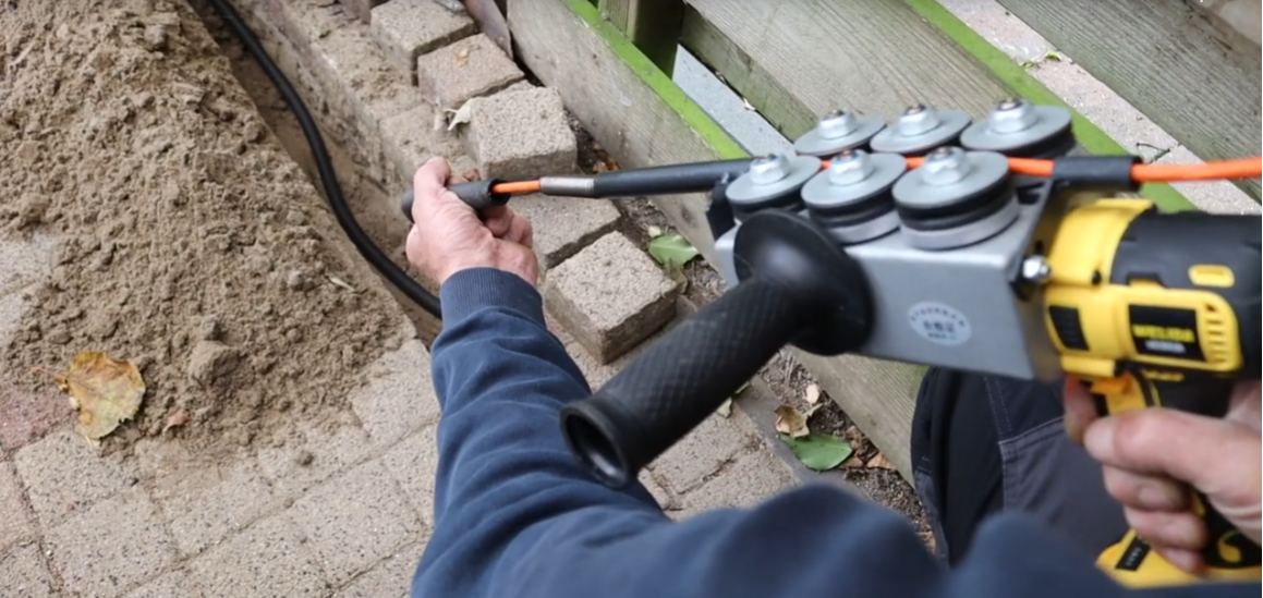 Monteur boort met speciaal gereedschap een kabelroute door de tuin