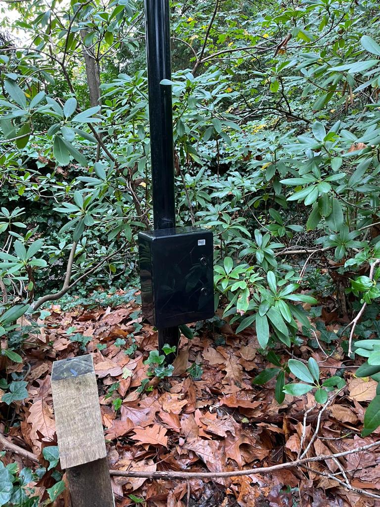 Buitenpaal met een grijze aansluitkast voor een camera op een terrein