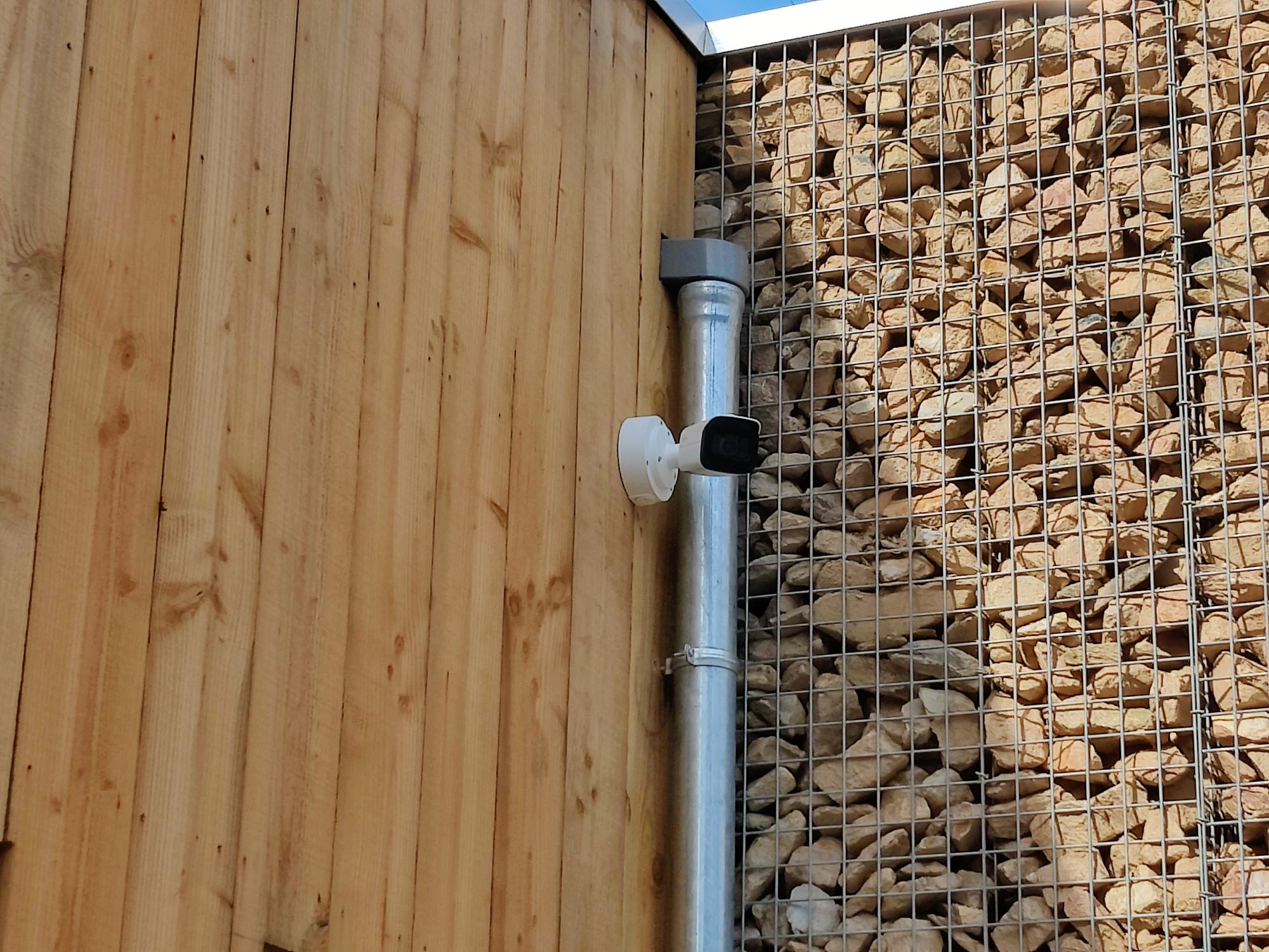 Camera tegen een houten gevel naast een schanskorfmuur