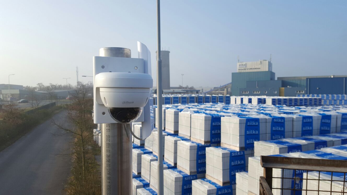 Bewakingscamera op een paal die uitkijkt over een industrieterrein vol opgestapelde bouwmaterialen