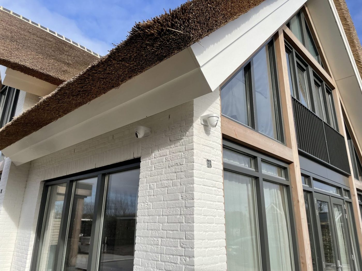 Beveiligingscamera van CameraInstallatie, netjes weggewerkt onder de rieten dakrand van een woning, zonder zichtbare kabel
