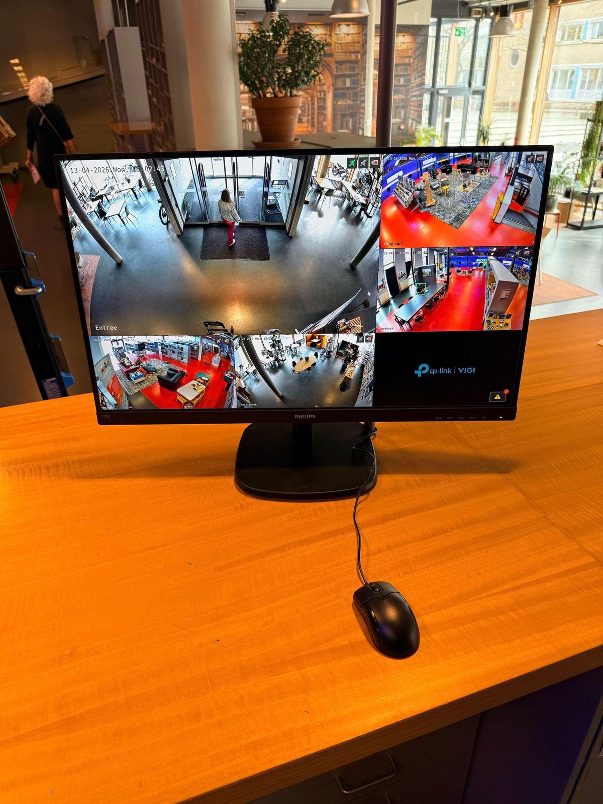 Monitor op de houten balie van een bibliotheek met live beelden van de entree en de leeszaal