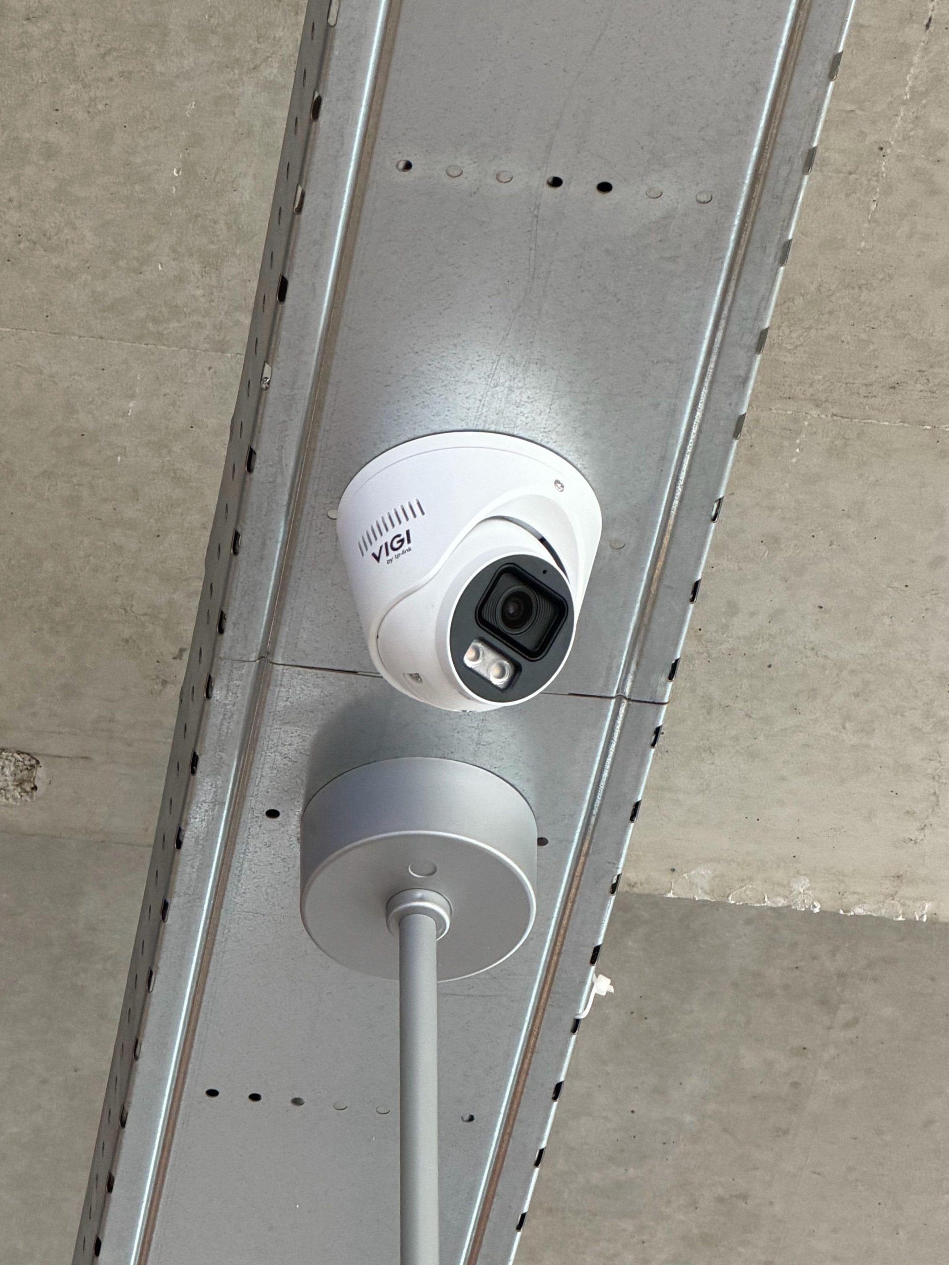Witte VIGI-turretcamera aan een kabelgoot onder een betonnen plafond