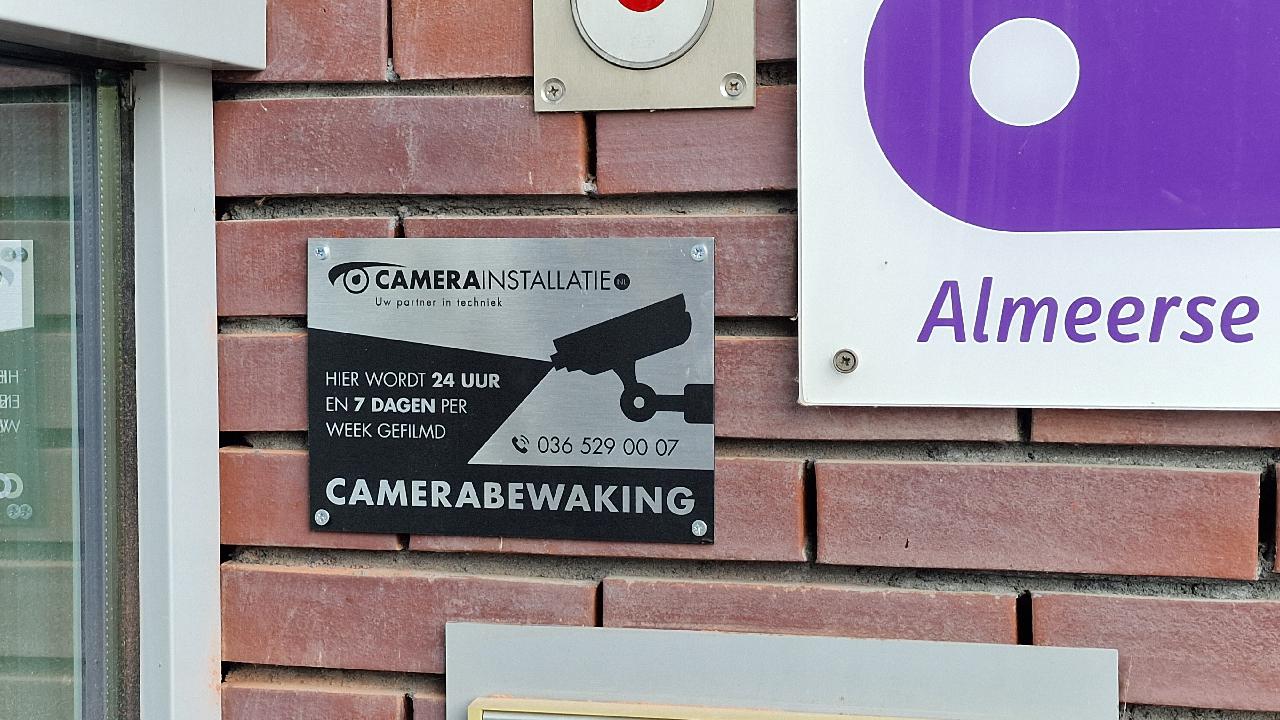 CameraInstallatie-bord Camerabewaking naast het naambord van een school bij de ingang